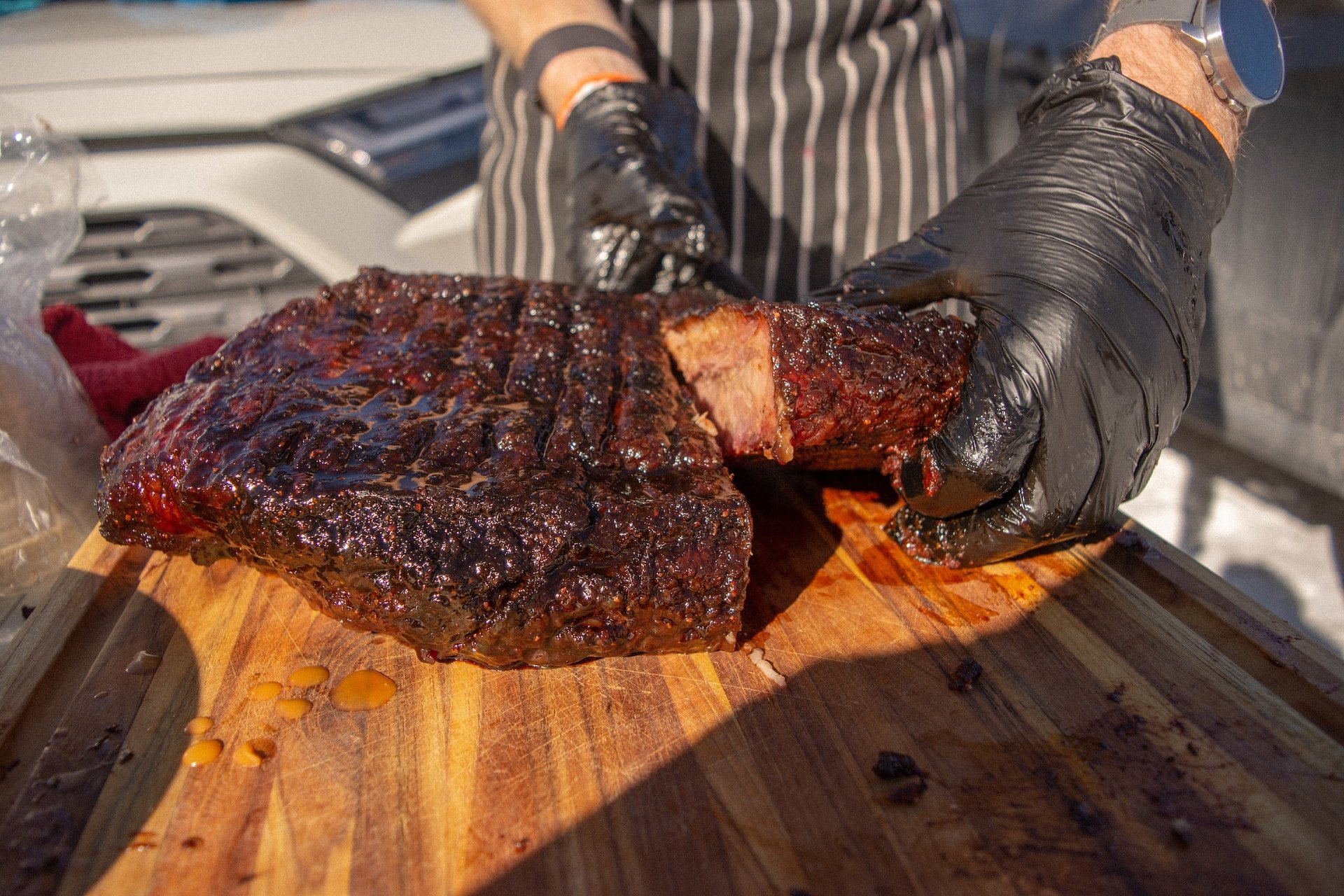 gloved hand holding a smoked brisket on a cutting board