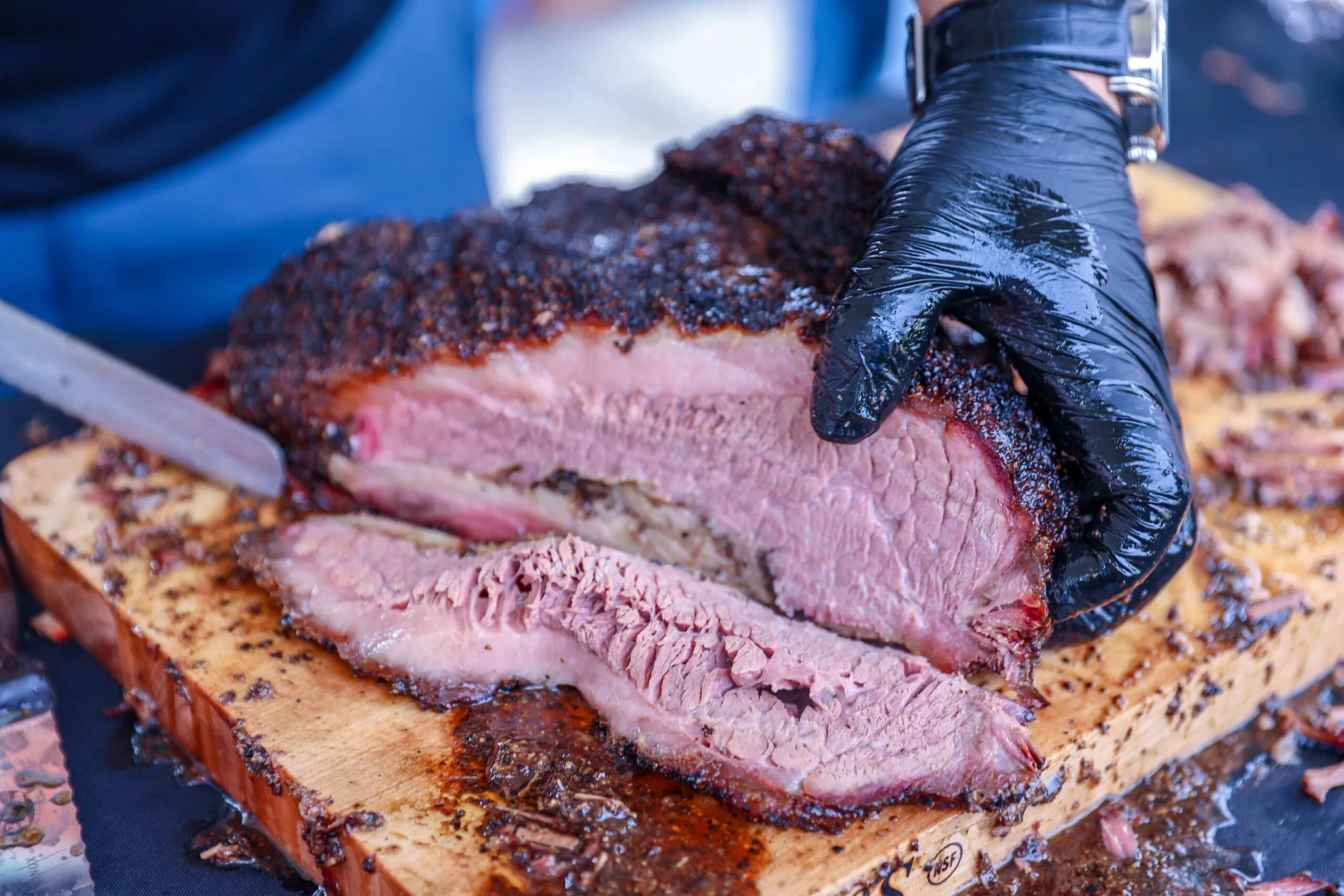 gloved hand slicing a smoked brisket showing the pink inside