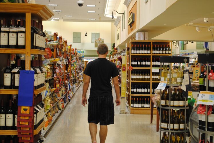 man in shorts walking into the wine section of a grocery store