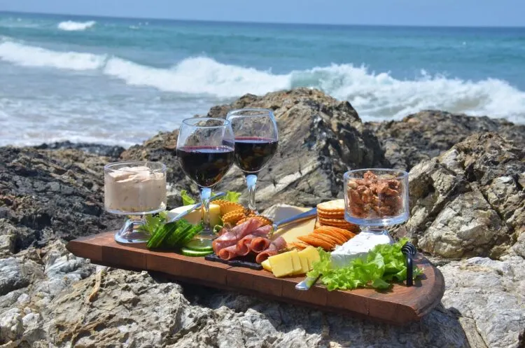 platter of meats and cheeses and red wine placed on rocks near the ocean